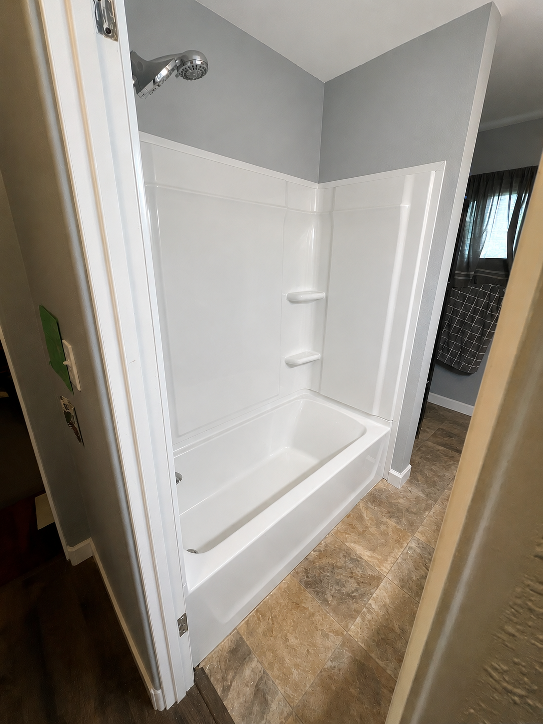 White tub and shower surround with beige tile floor in a Cedar Valley bathroom