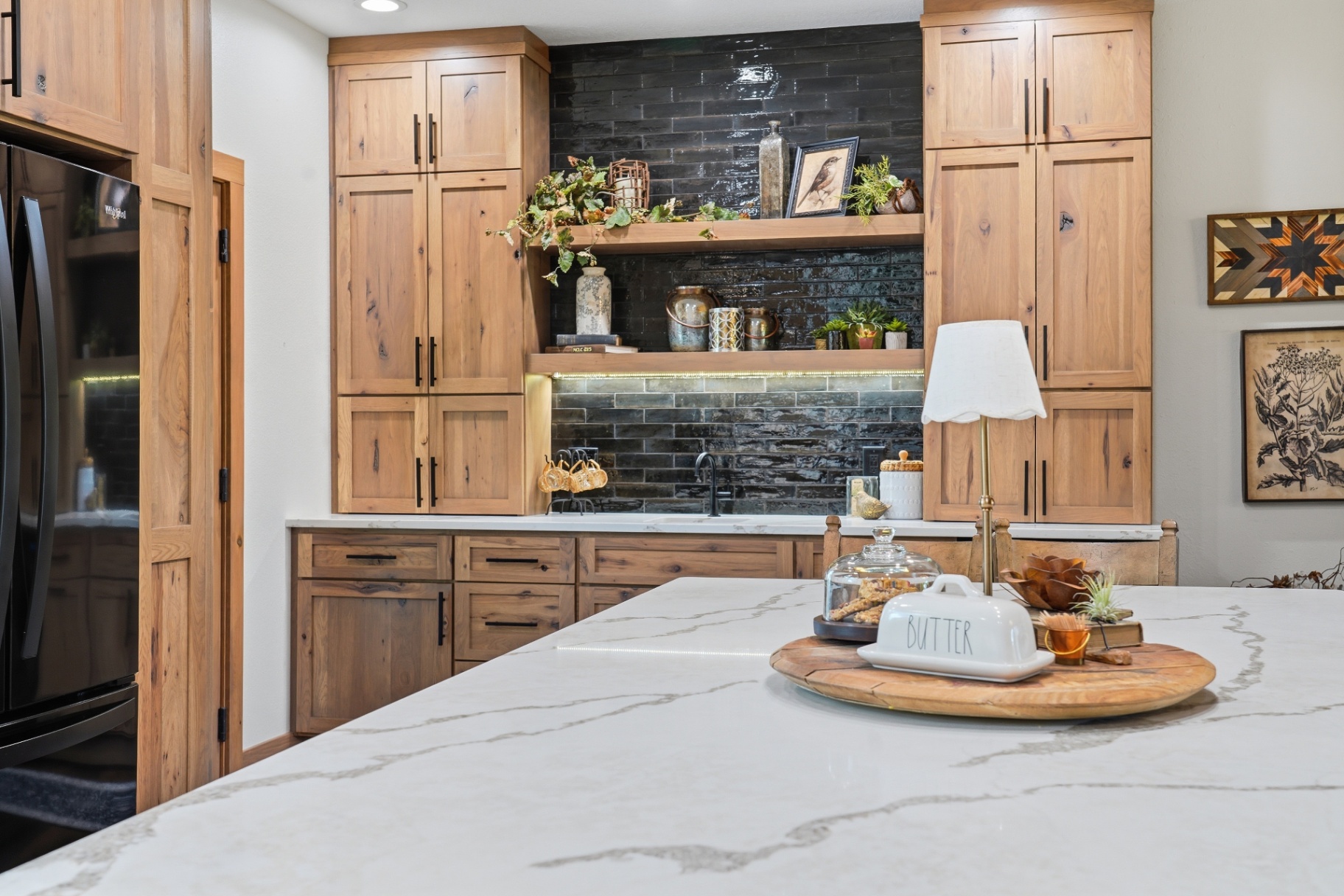 Wet bar open shelving with glossy black tile viewed across the kitchen island