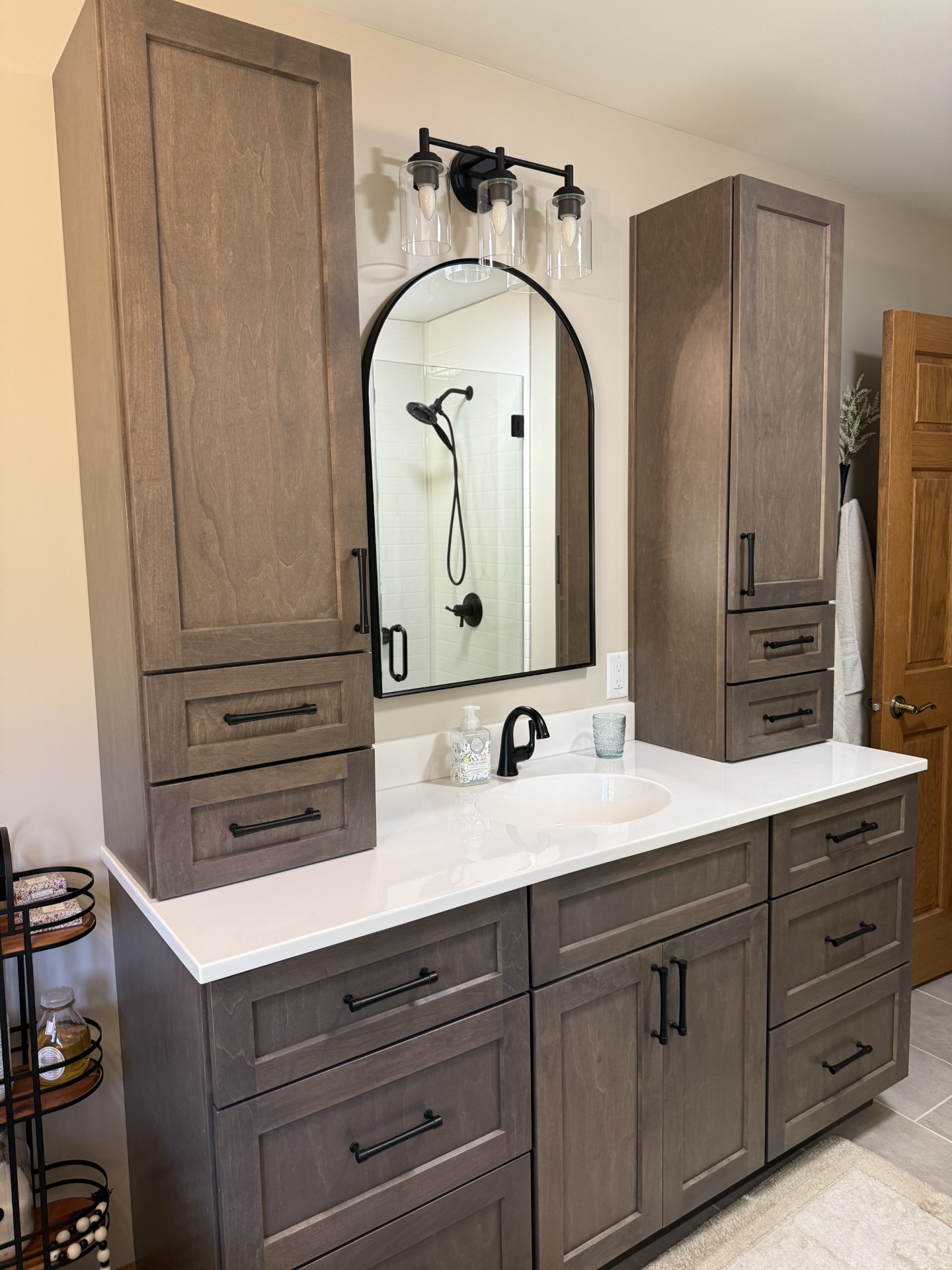 Custom stained maple Countryside vanity with integrated Onyx Glacier top, arched black mirror, and matte black Delta fixtures