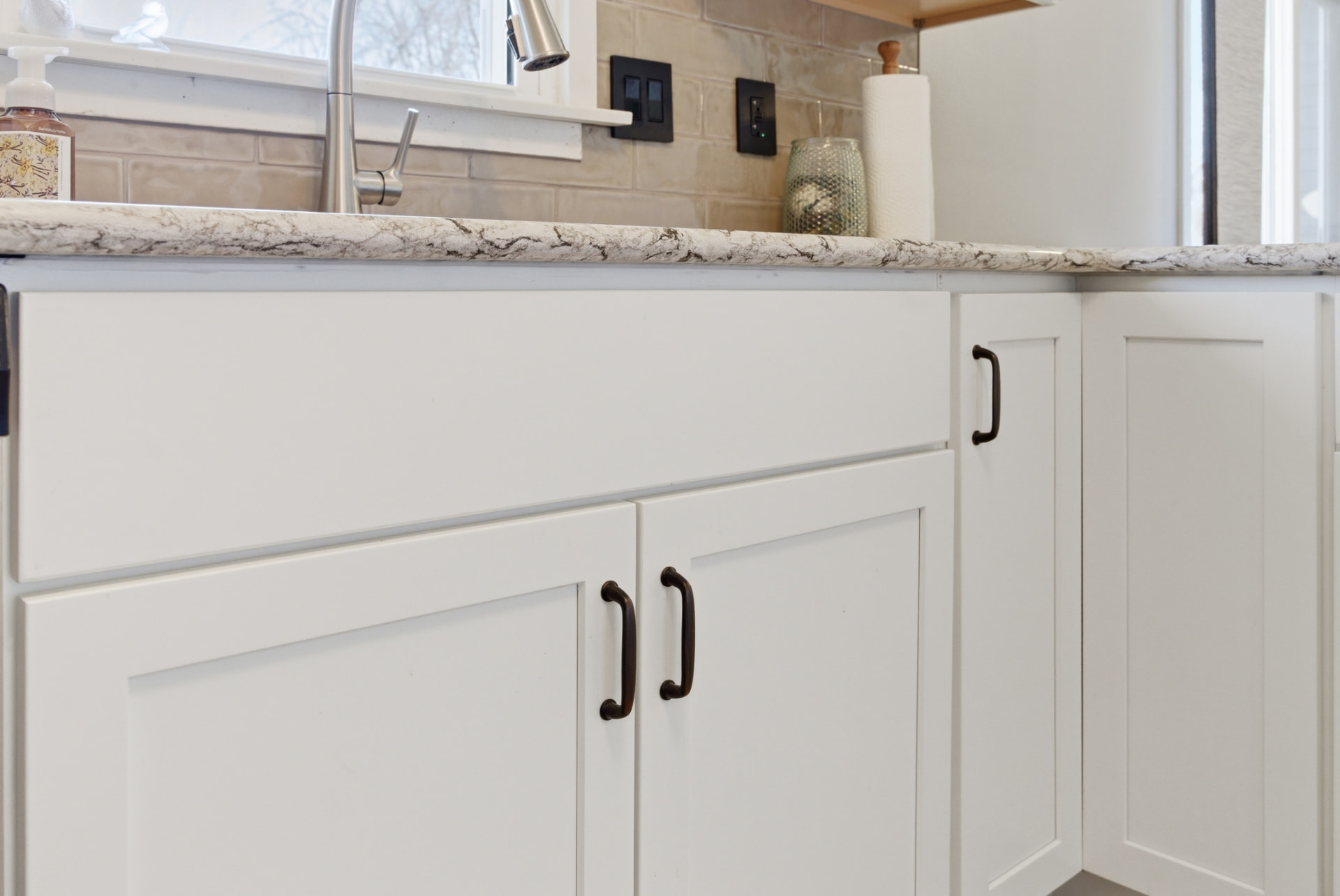 Close view of the white sink cabinet, countertop edge, and tile backsplash