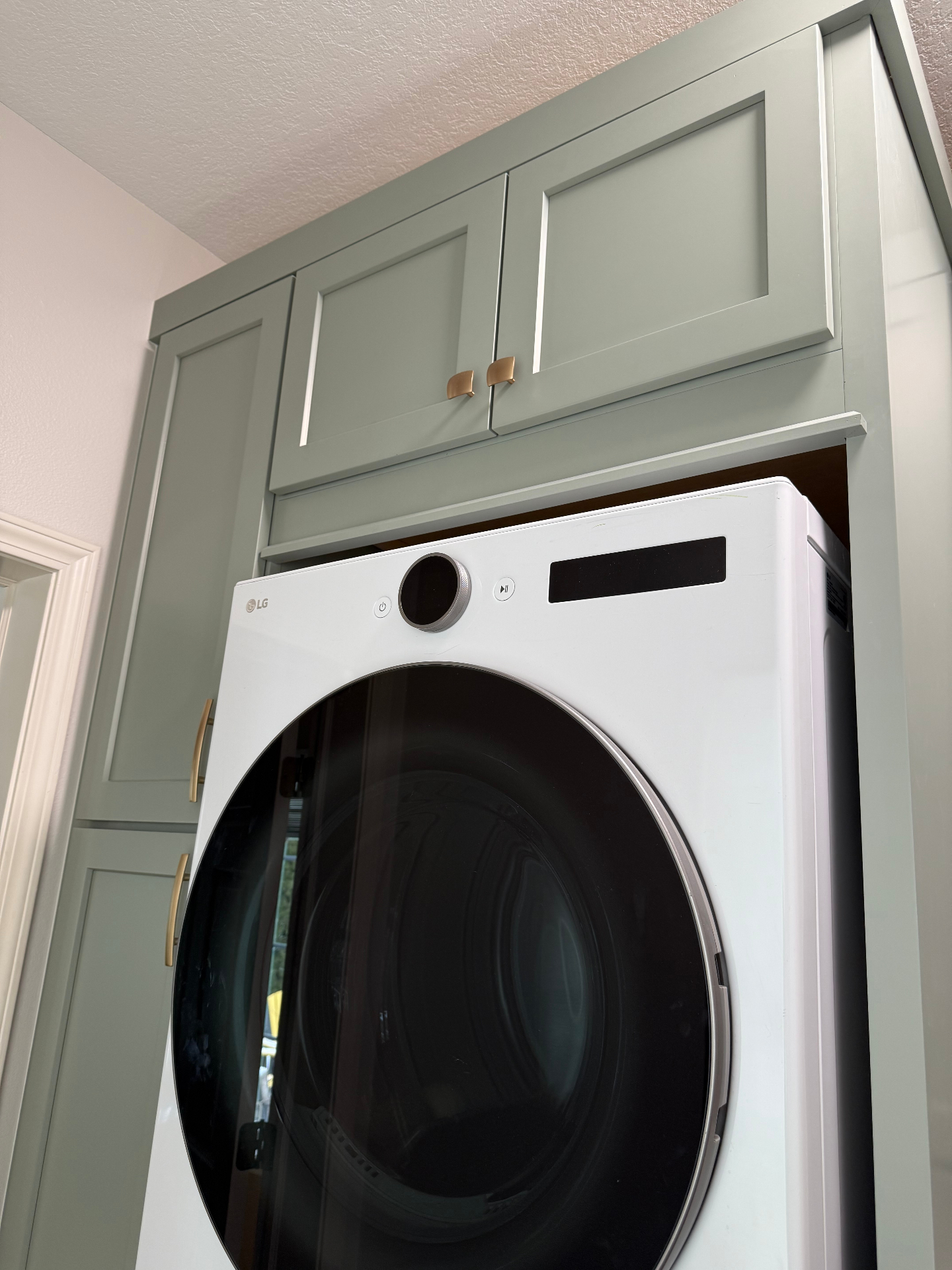 Upper sage cabinetry detail above stacked LG washer and dryer with brass hardware