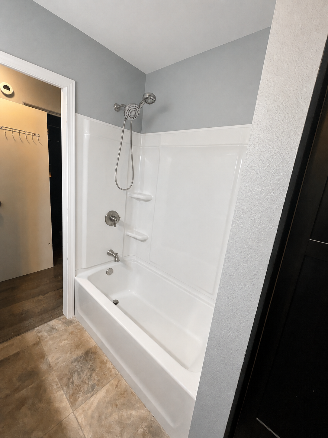 New brushed nickel shower handle, tub spout, and shower head installed on white tub surround