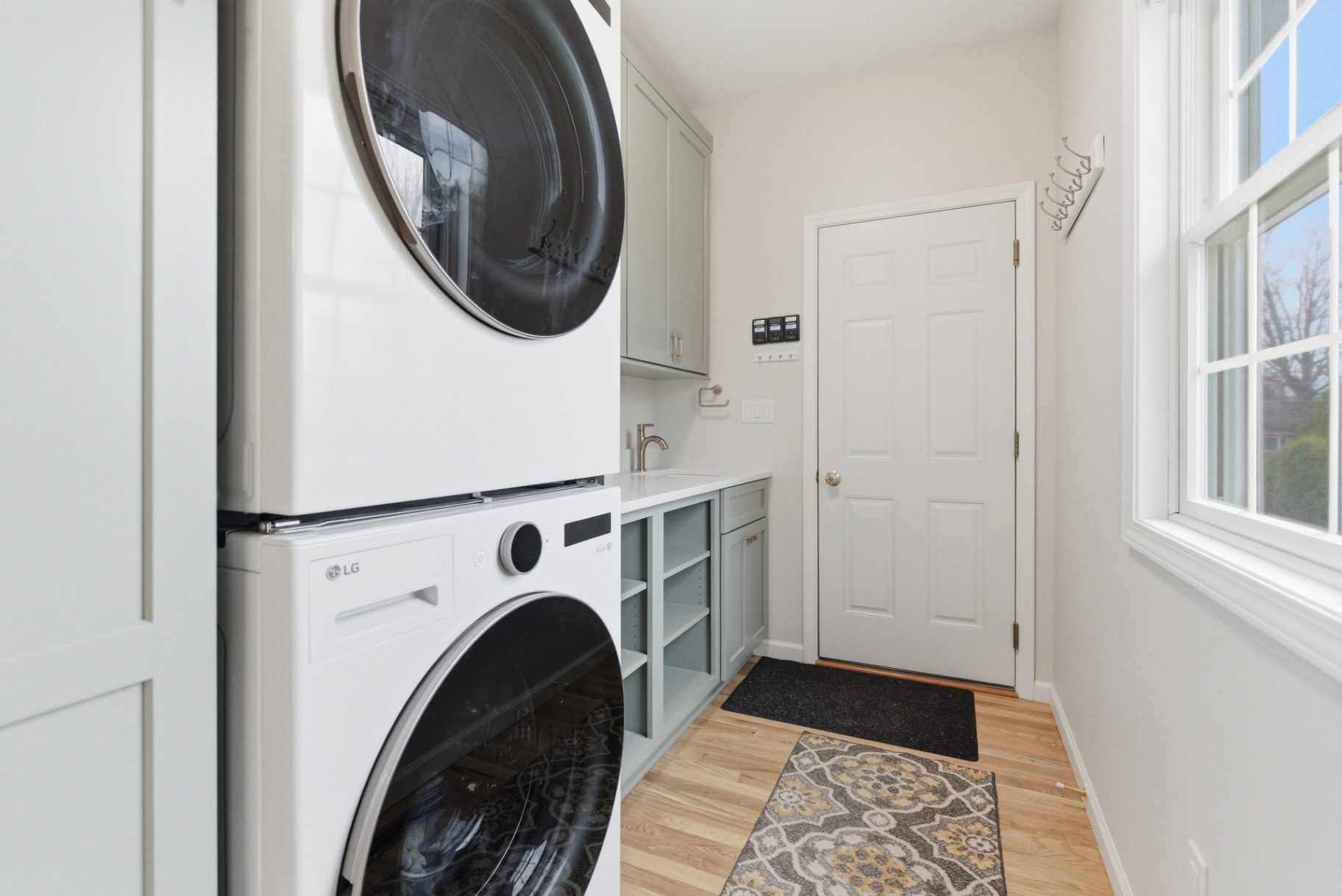 Finished Waterloo laundry room with stacked washer and dryer, sage cabinetry, and utility sink