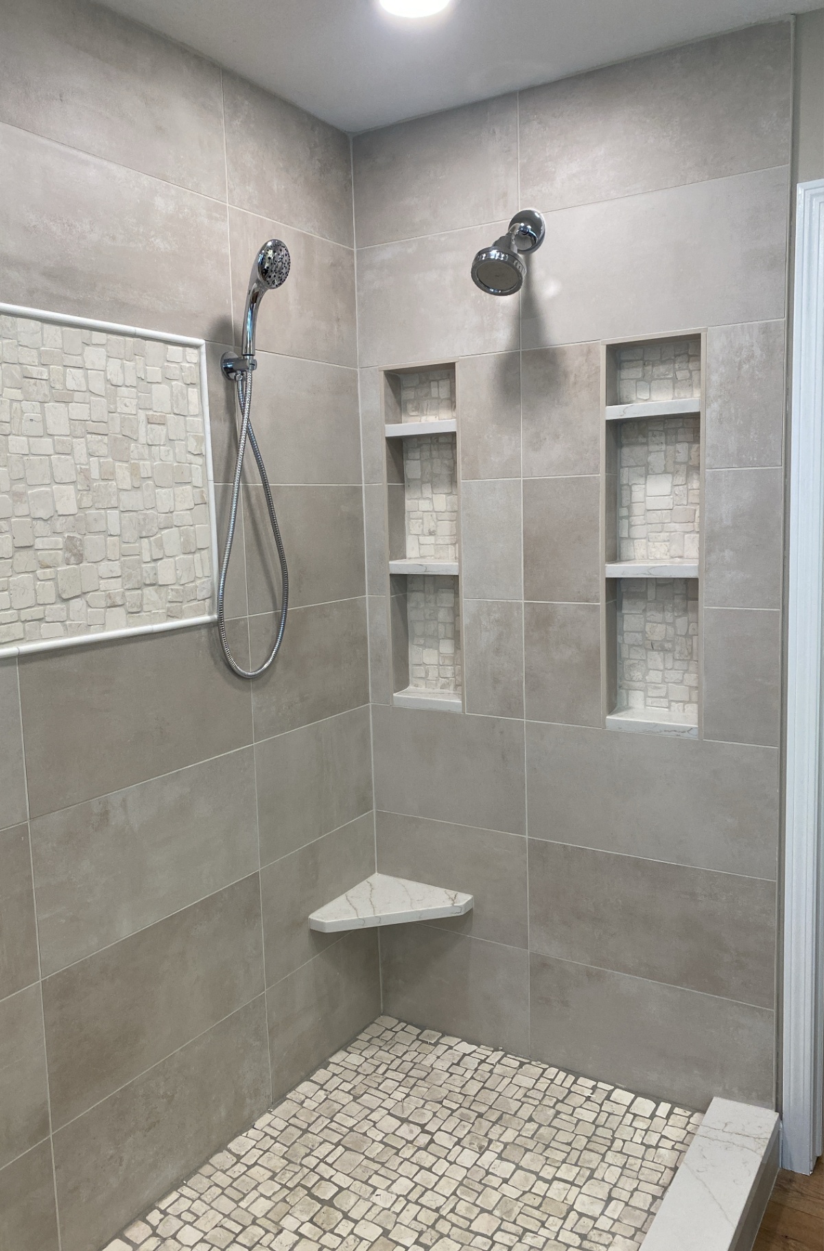 Close view of the finished Cedar Falls walk-in shower with large-format tile, stone niche accents, and a corner bench