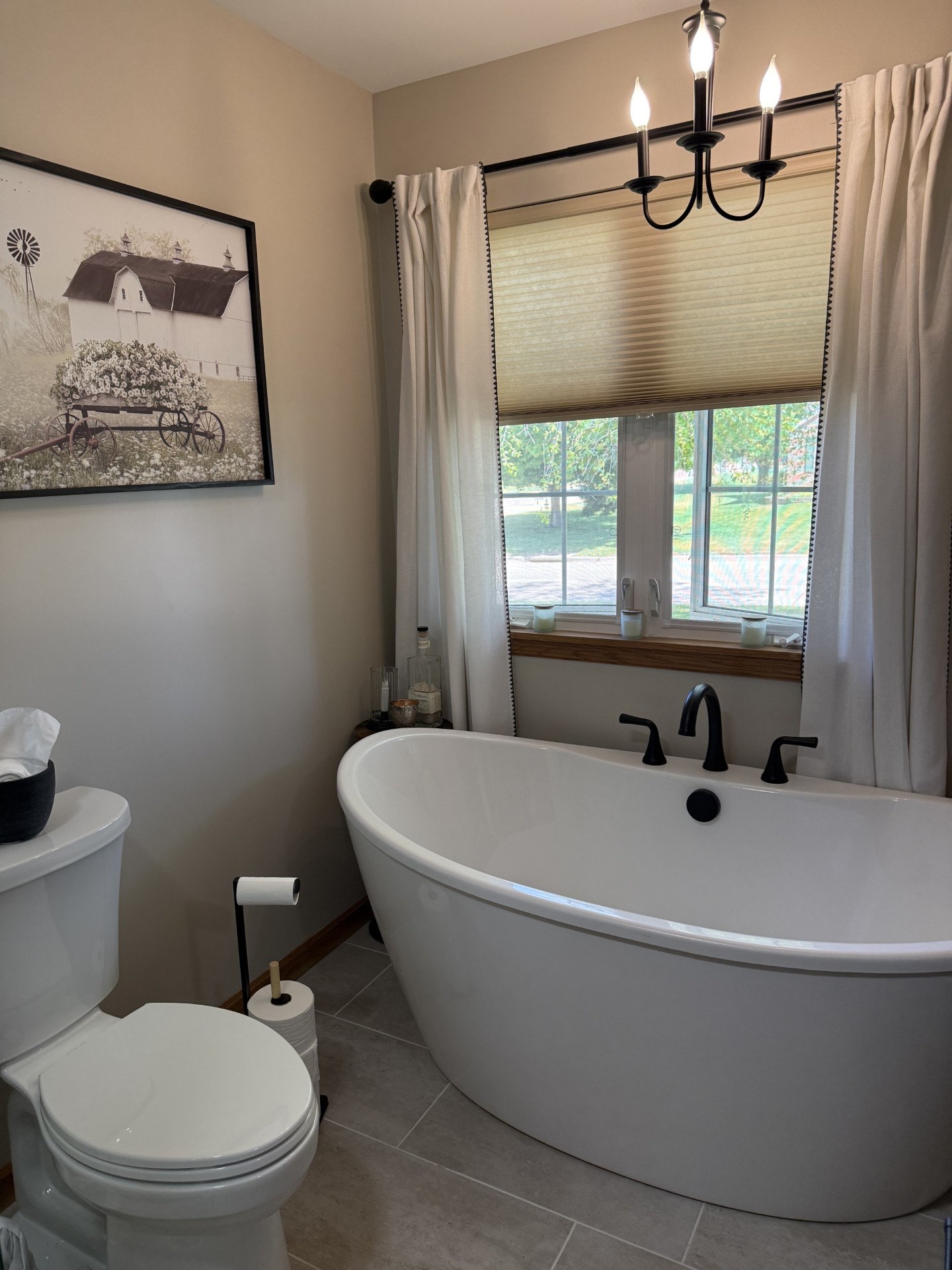 Freestanding soaker tub under a window with matte black Delta tub filler and black chandelier overhead
