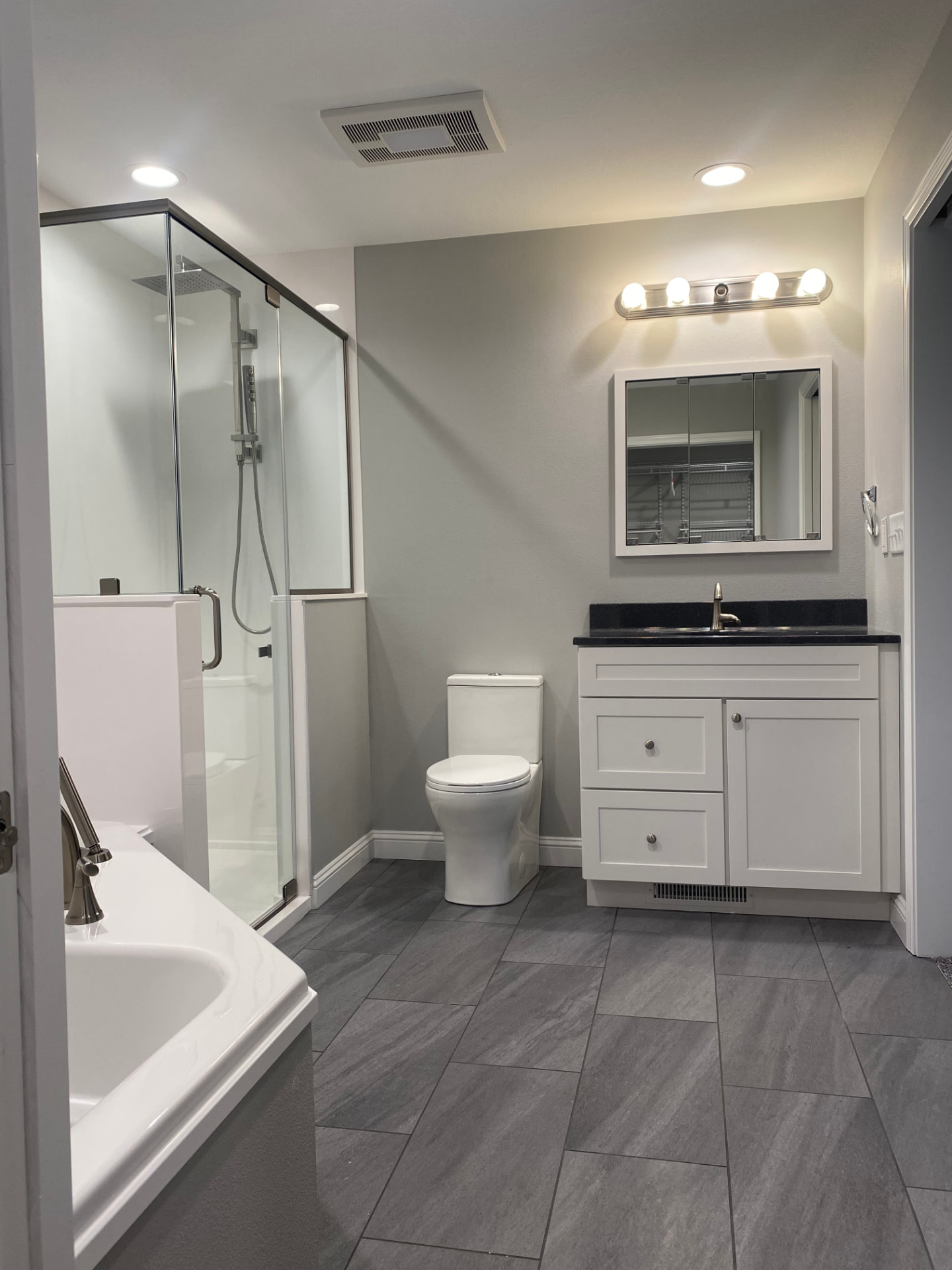 Bathroom with gray tile floor, white vanity, tub, and glass shower