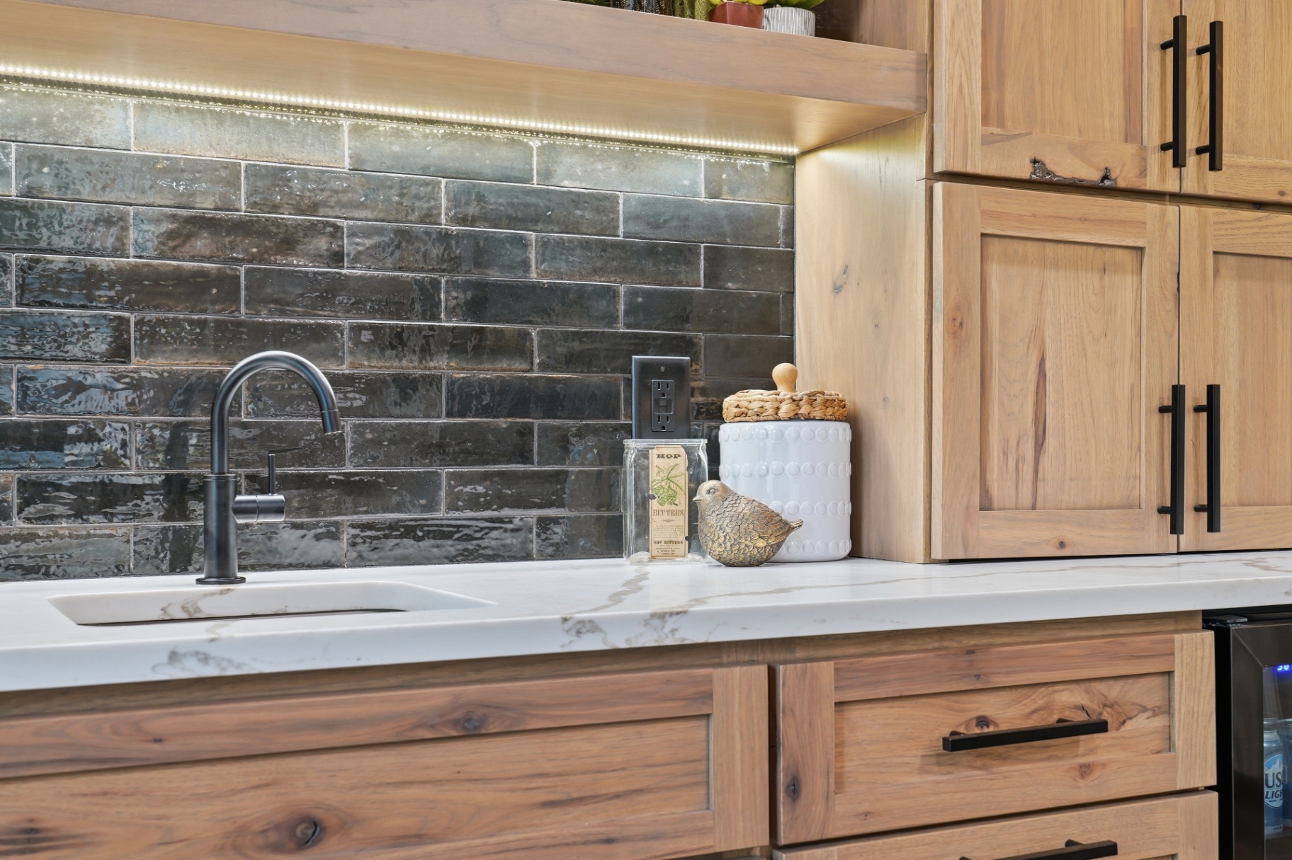 Detail of the wet bar's glossy black elongated subway backsplash and quartz counter