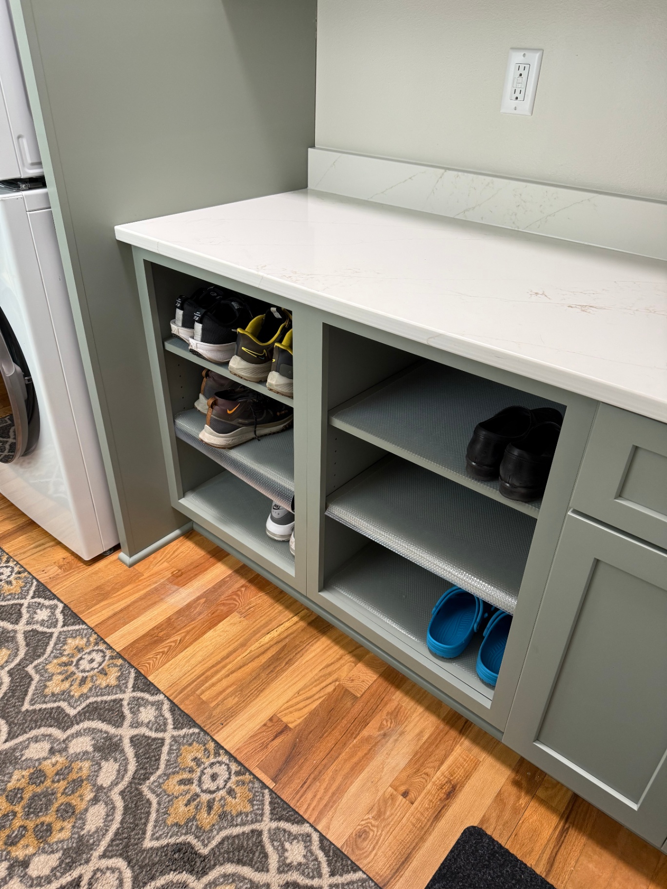 Custom shoe storage cubbies in sage cabinetry with quartz counter above